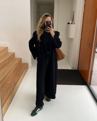 Black trouser outfits: @anoukyve wears a long black coat with tailored trousers and trainers