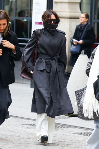 Victoria Beckham wearing a black funnel-neck coat with white pants and platforms heels in Paris