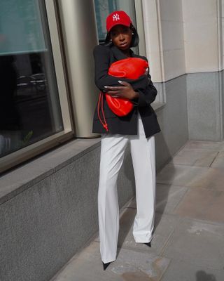 Ama Godson in a red hat, black blazer, and white trousers with a red clutch bag.