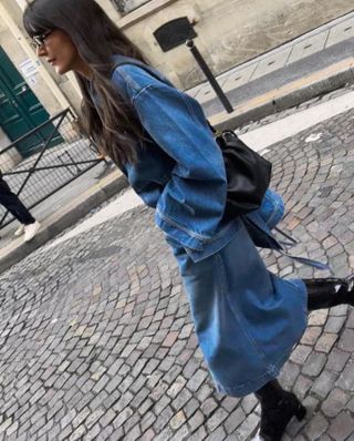 Woman wearing denim jacket, denim skirt, and black boots while standing on Paris street.