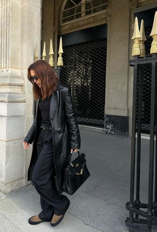 best suede boots shown on a photo of a woman at a park in paris wearing a black leather coat over a crewneck sweater with matching black trousers and brown suede chelsea boots and a black handbag