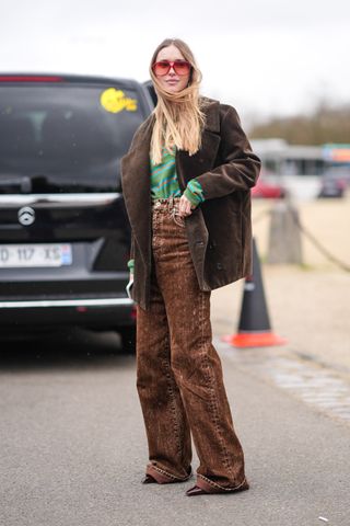 A woman wears a brown corduroy blazer with brown jeans and a green and red striped shirt.