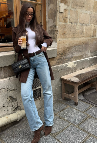 best suede boots shown on a photo of a woman standing outside a cafe wearing a dark brown suede coat over a white long-sleeve t-shirt with straight-leg jeans and brown pointed ankle boots