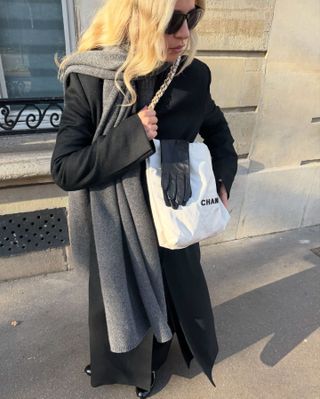 Patent leather Chanel moccasins seen on Stephanie Broek alongside a long black wool coat, gray scarf, white Chanel bag, and leather gloves.