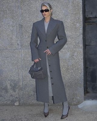 @hoskelsa wearing a Helsa grey hourglass maxi coat with grey socks, black pumps, and a grey handbag