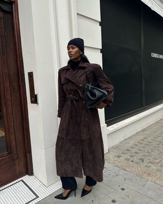 fashion influencer @nlmarilyn wearing a brown suede trench coat with a black The Row Margaux Bag, black beanie, and black pumps