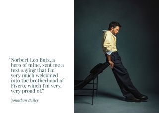 Jonathan Bailey leans against a chair wearing a Zegna yellow and blue layered shirt with black trousers.