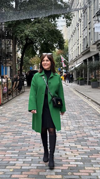 A former Nordstrom buyer wearing a long green coat over a black skirt.