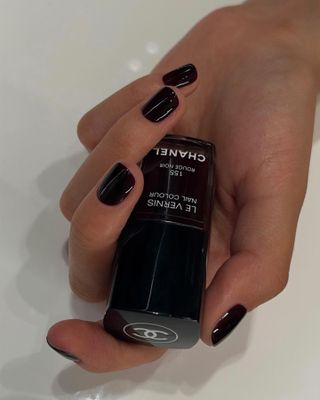 Burgundy nails holding Chanel rouge noir nail varnish bottle