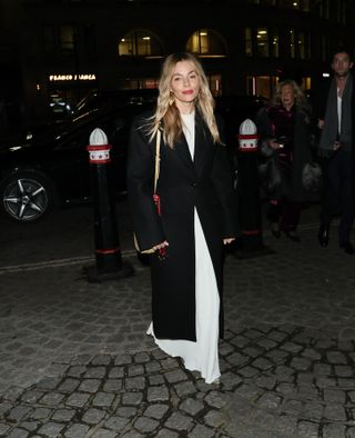 Sienna Miller in a black coat with a white dress and snake print boots