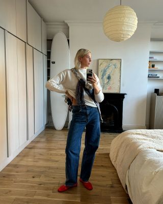 London woman wears a white knit mock-neck sweater, Slvrlake jeans, and red Dear Frances Balla Flats.