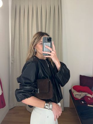 Eliza Huber in the dressing room at Madewell's new SoHo flagship in New York wearing a cropped leather balloon-sleeve jacket with wide-leg white jeans, brown suede loafers, and a brown suede bag.