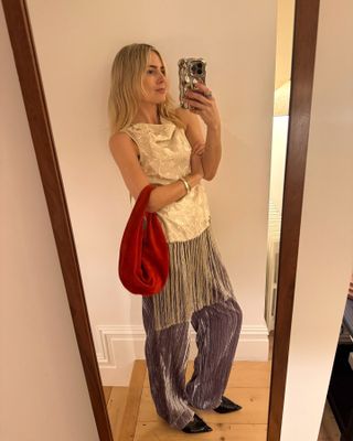 British style influencer Lucy Williams poses for a mirror selfie with a silver iPhone case wearing a party outfit with sleeveless fringe top from Sea, red velvet bag, an purple velvet pants