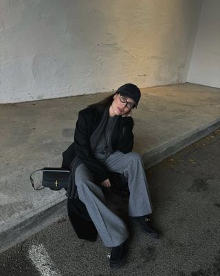 @annabelrosendahl wearing grey trousers, jumper and long black coat