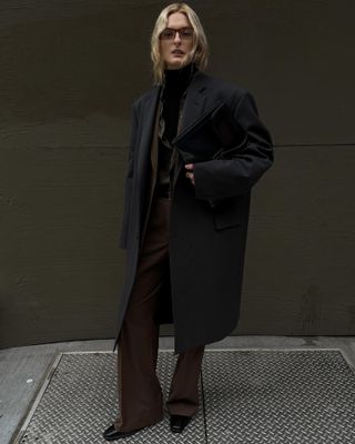 Woman wearing long black coat, brown pants, and brown blazer in SoHo.