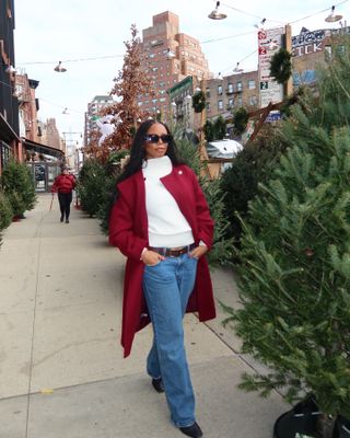 Woman wearing cashmere sweater, red coat, blue jeans and black sunglasses while walking on New York City street.