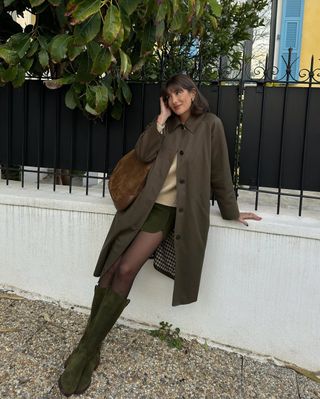 @juliesfi wearing a mini green skirt with boots and trench