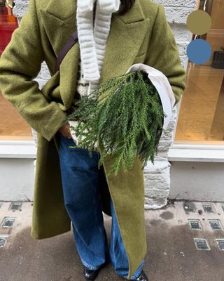 girl carrying a plant wearing a green coat worn with blue baggy jeans