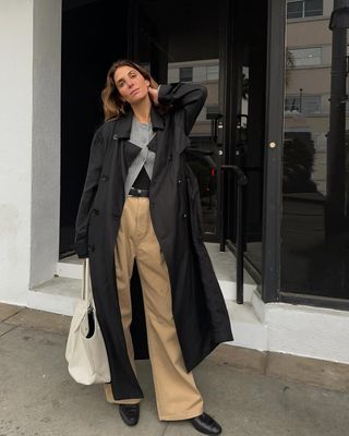 Jen Azoulay in a black trenchcoat, khaki pants, and loafers.