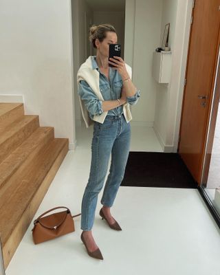 Anouk Yve in a denim shirt, jeans, and a sweater over the shoulders.