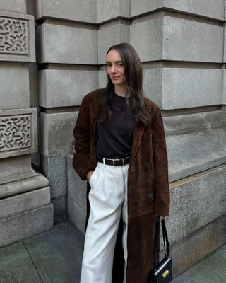 Olivia Perez wearing a brown suede trench coat with a black sweater and white jeans.