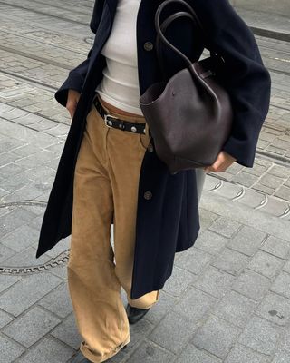 Woman wearing corduroy pants, white shirt, navy coat and brown leather bag.