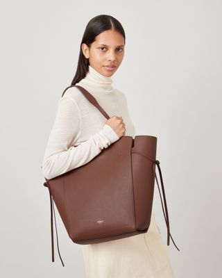 Woman wears cream turtleneck and carries brown tote bag