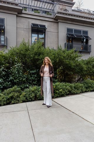 A Nordstrom stylist wearing a long brown coat with a powder pink sweater and white jeans.