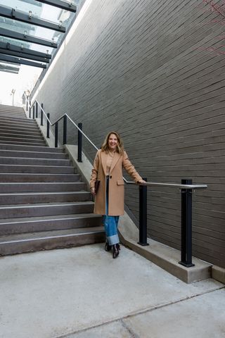 Woman wearing a long tan coat with cuffed blue jeans.