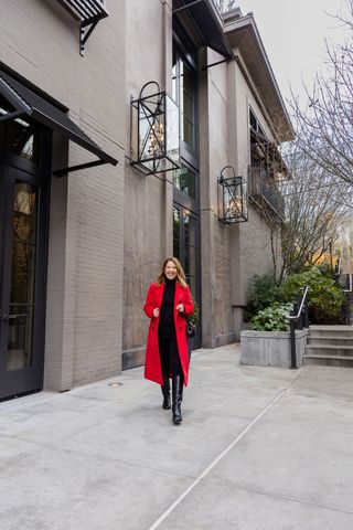 Woman wearing a long red coat with a black top, black jeans, and tall black boots.