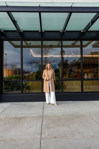 A Nordstrom stylist wearing a long tan coat with a tan sweater and white jeans.