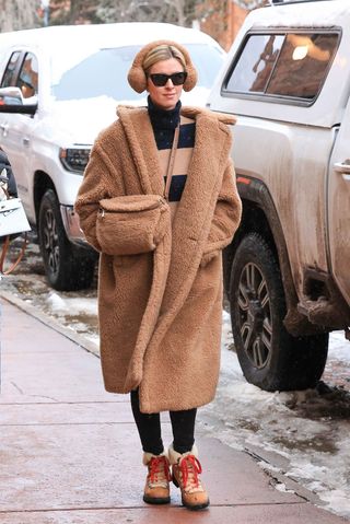 Nicky Hilton wears fur ear muffs, a brown and tan striped sweater, teddy coat, fur bag, black leggings, and combat ankle boots.