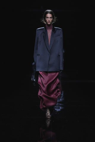 Model at the Khaite F/W 24 runway show wearing a black satin blazer with a burgundy satin skirt.