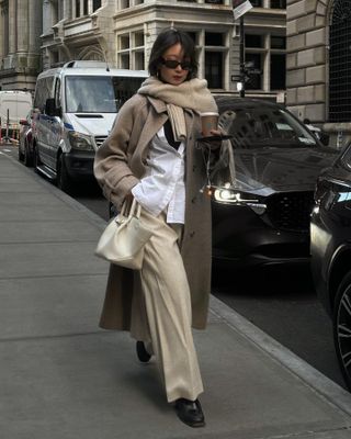 @thecarolinelin carries a cream top-handle bag whilst wearing a beige coat and cream trousers