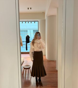 Eliza Huber wearing a white sheer scarf blouse with a brown pleated skirt at the Carven store in Paris.