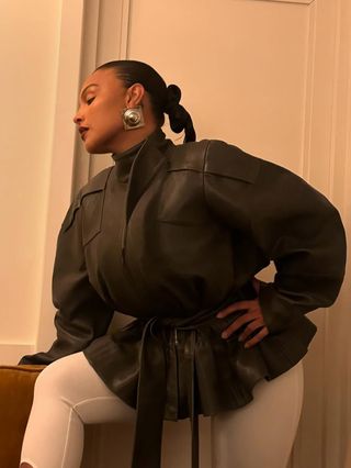 Paloma Elsesser wearing '80s earrings, a leather belted jacket, and white leggings.