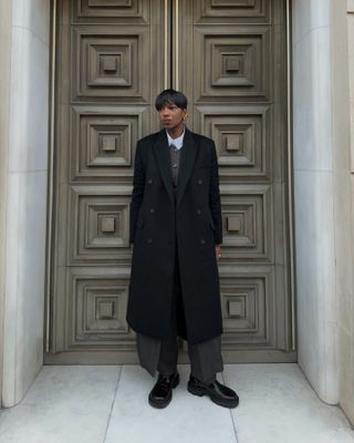 Woman wearing gray sweater, black coat, and black chunky boots.