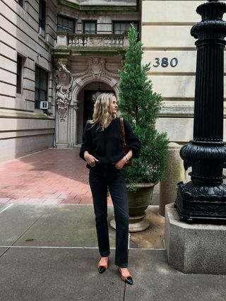 Eliza Huber wearing a black V-neck sweater, brown bag, black Citizens of Humanity Zurie black jeans, and brown shoes.