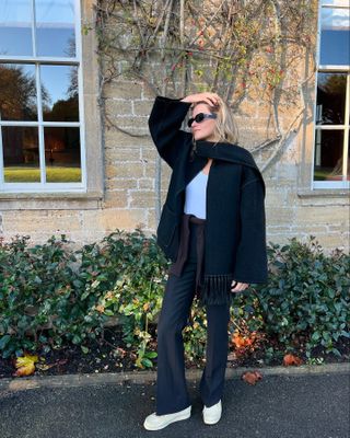 Eliza Huber wearing Clarks Wallabee shoes with a black Toteme coat, white tank top, and black Gucci trousers at Babington House in England.