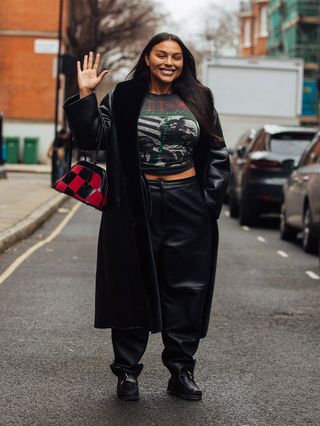 LONDON, ENGLAND - FEBRUARY 20: Model Paloma Elsesser waves and wears a black leather trench, black Martin Luther King Jr. shirt, black leather pants, black leather Clark's Wallabee shoes, and carries a black and red checkered purse after the 16Arlington show at Yeomanry House during London Fashion Week Fall/Winter 2022 on February 20, 2022 in London, England.