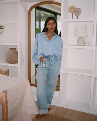 British fashion influencer Monikh Dale poses in her chic London home wearing a blue button-down and light-wash cuffed jeans.