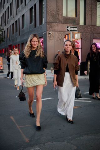 Eliza Huber and Lauren Eggertsen at the S/S 25 Tory Burch show wearing sporty utilitarian jackets with formal dresses and skirts.