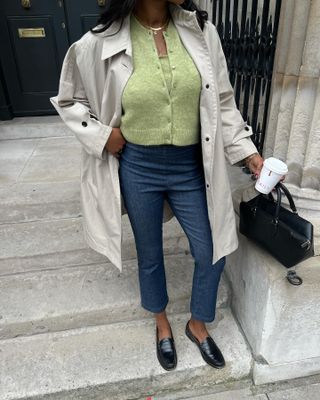 Georgia wears a trench coat, green cardigan, cropped pants, loafers, and the black patrizia reformation bag.