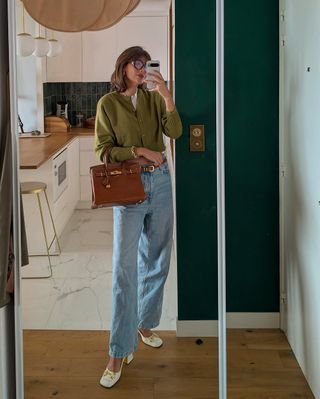 @juliesfi wears an olive green cardigan, straight-leg jeans and white heeled ballet flats