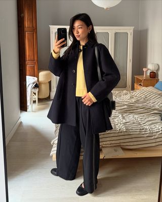 @michellelin.lin wears a yellow jumper with a black coat, relaxed trousers and ballet flats