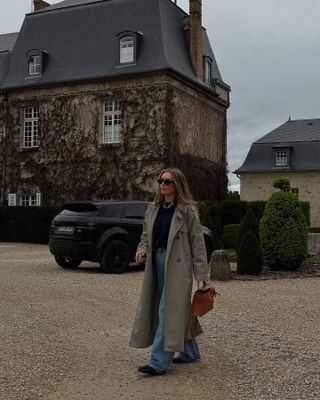 Woman wearing a trench coat over a black sweater and jeans.