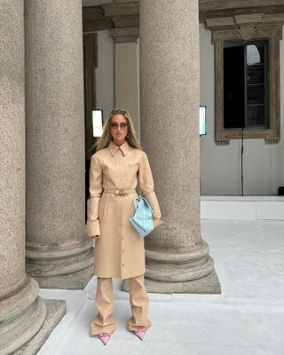 Woman wearing nude tan leather coat, matching leather pants, and baby blue Bottega Veneta bag