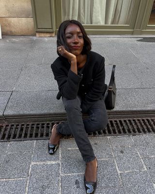 @aidabadji_ wears black skinny jeans with a boucle jacket and ballet flats while sitting on a pavement