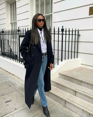 Woman wears black coat, white shirt, blue jeans and black boots