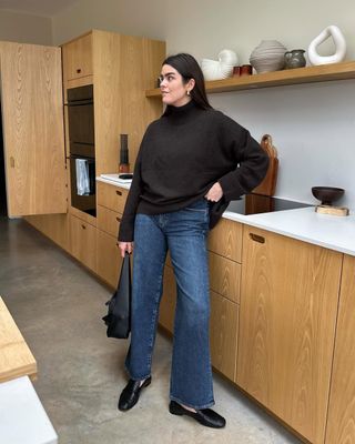 Woman wears brown jumper, blue jeans and black loafers